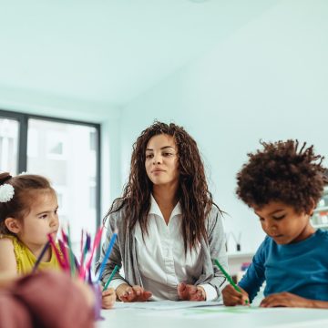 Teacher and adorable children being creative with colorful pencils at kindergarten