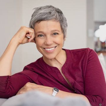 Portrait of smiling senior woman relaxing on couch at home. Happy mature woman sitting on sofa and looking at camera. Closeup of lady relaxing at home.